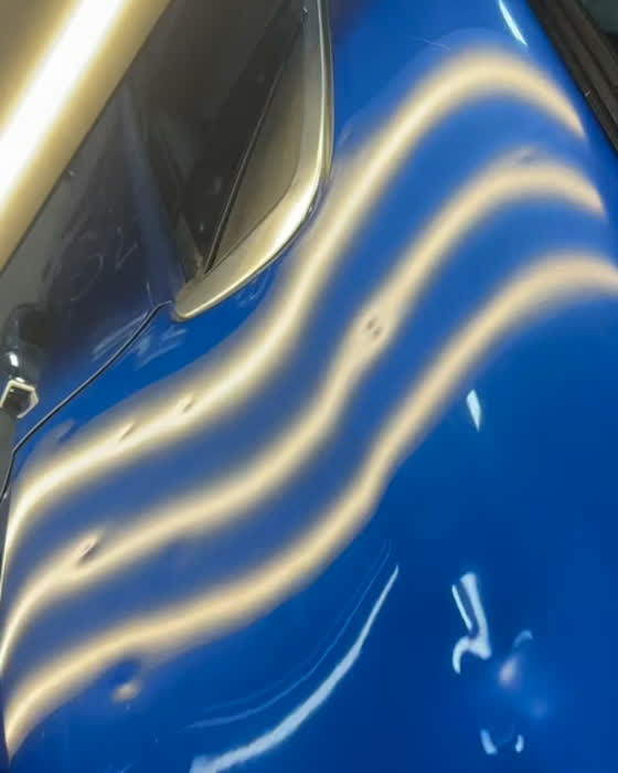 Hail dents bending the reflected light lines on a blue panel