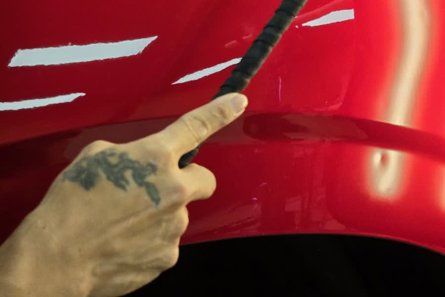 A technician points to a dent the light reveals on a red panel
